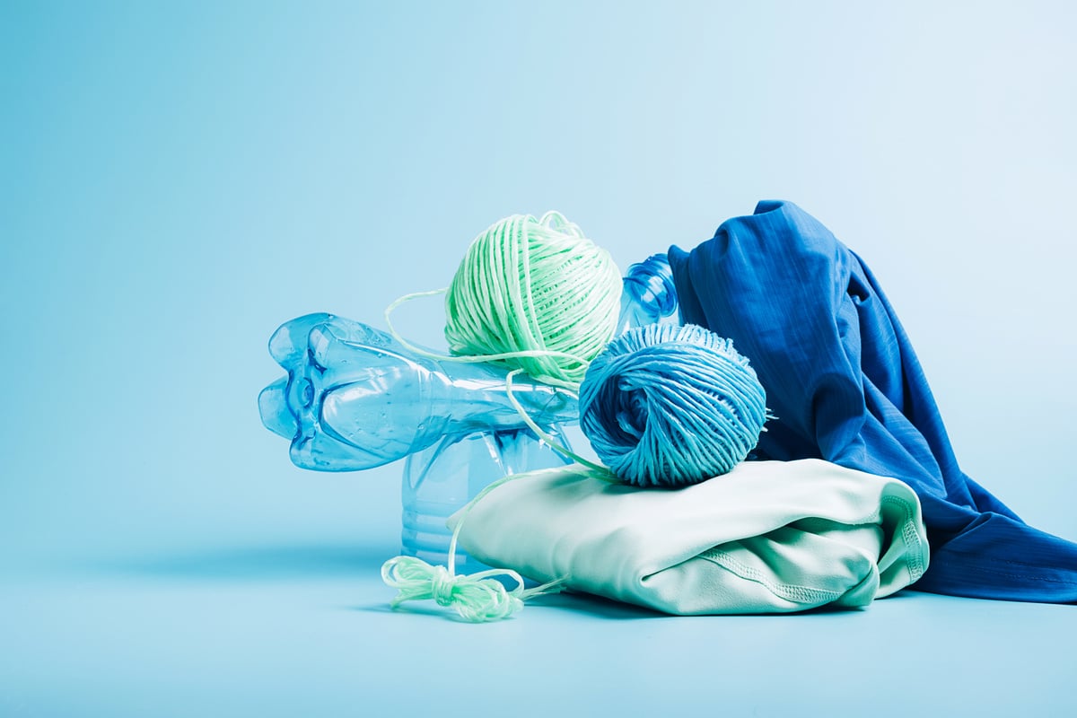 Empty Plastic Bottle and Various Fabrics Made of Recycled Polyester Fiber Synthetic Fabric on a Blue Background